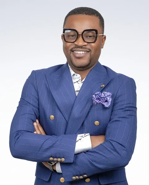 Professional headshot of a man in a blue double-breasted blazer with arms crossed, smiling at the camera